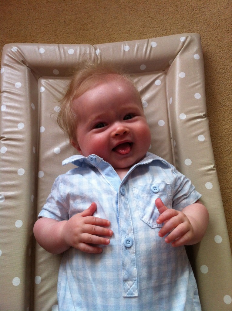 baby fashion, Lucas lying down smiling at the camera wearing a blue and white cotton checked romper suit