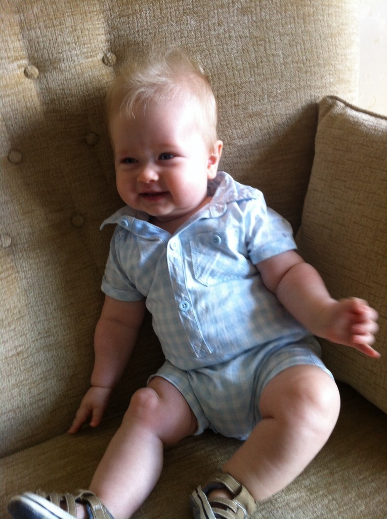 baby fashion, lucas sat on a cream sofa wearing a blue and white cotton checked romper suit