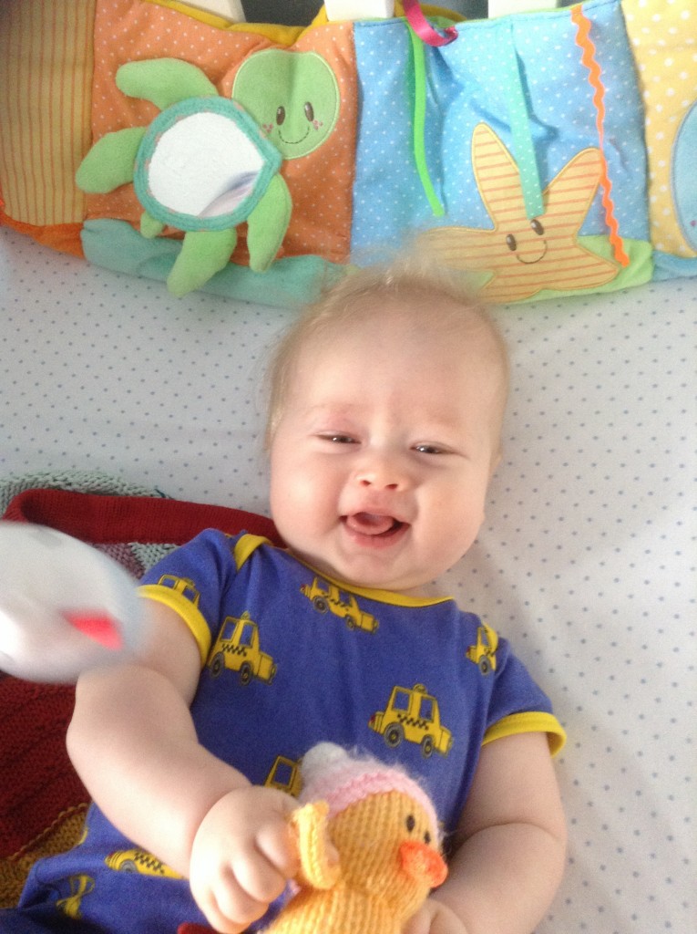 lucas as a baby looking up at camera smiling wearing a blue top with yellow cars on