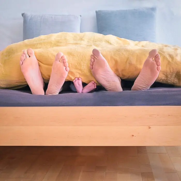 three pairs of feet showing at the end of the bed, 2 adults and 1 child