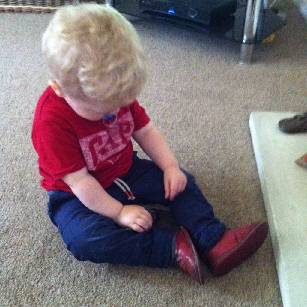 Lucas looking down at red shoes he is wearing. They are his uncles first shoes. Lucas is wearing a red gap t shirt and navy pants
