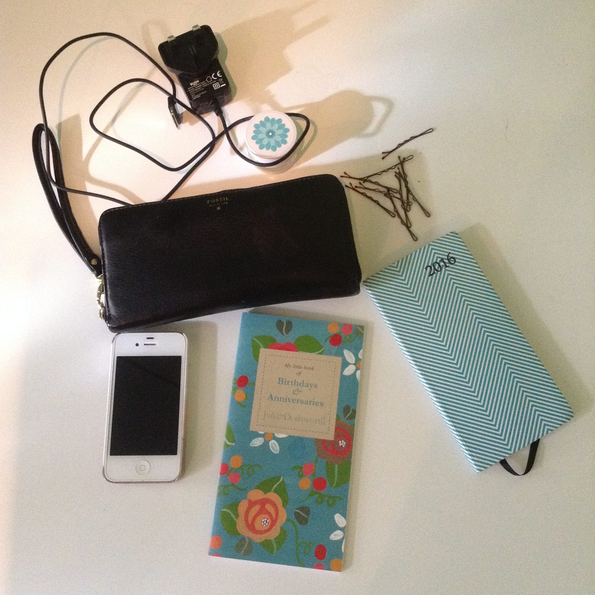 Blogtober, what's in my bag. Photo of white iPhone 4, julie Dodsworth floral birthday book, white and green stripy diary, black phone charger, brown kirby grips, black leather fossil purse, lip balm