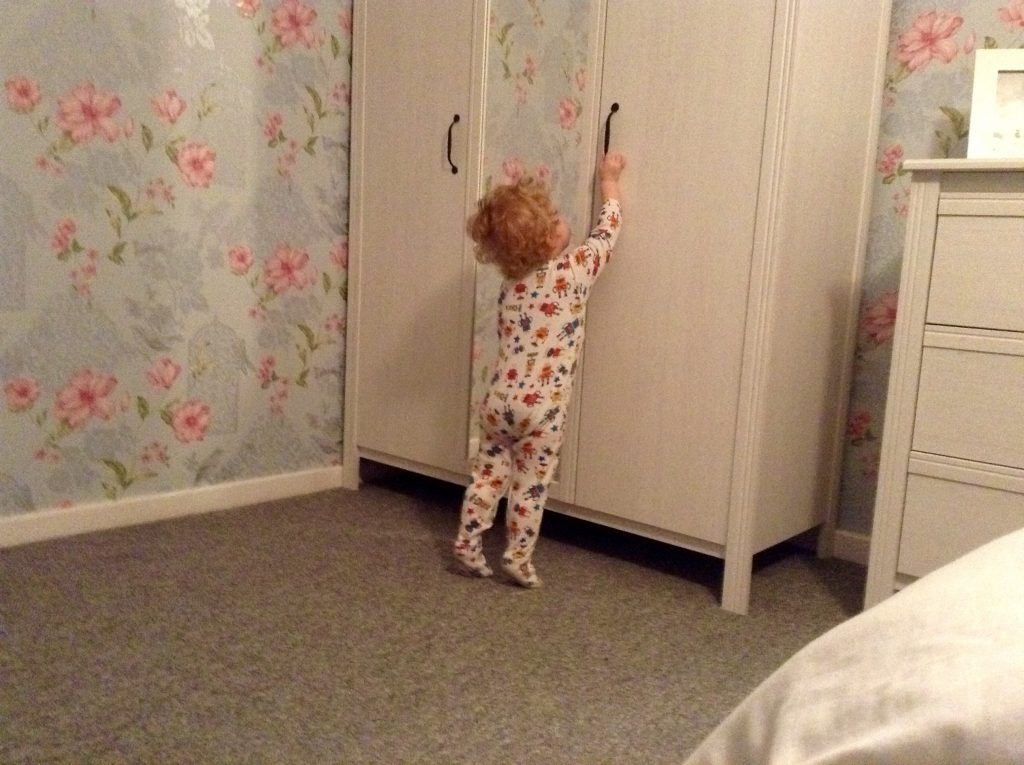 Ordinary moments Lucas reaching up to black handle on white wardrobe with floral wallpaper in the background and grey carpet 