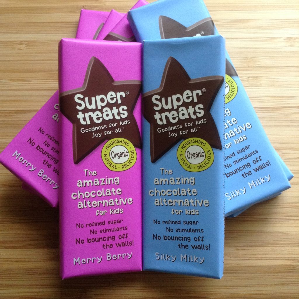 Supertreats review silky milky chocolate in blue wrapper and berry merry chocolate in pink wrapper on a wooden chopping board