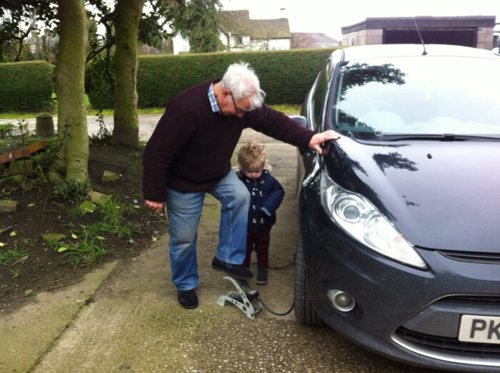 My Grandad learning with his hand against my black ford fiesta, his foot on the foot pump putting air into the front tyre with Lucas watching down at the side of him