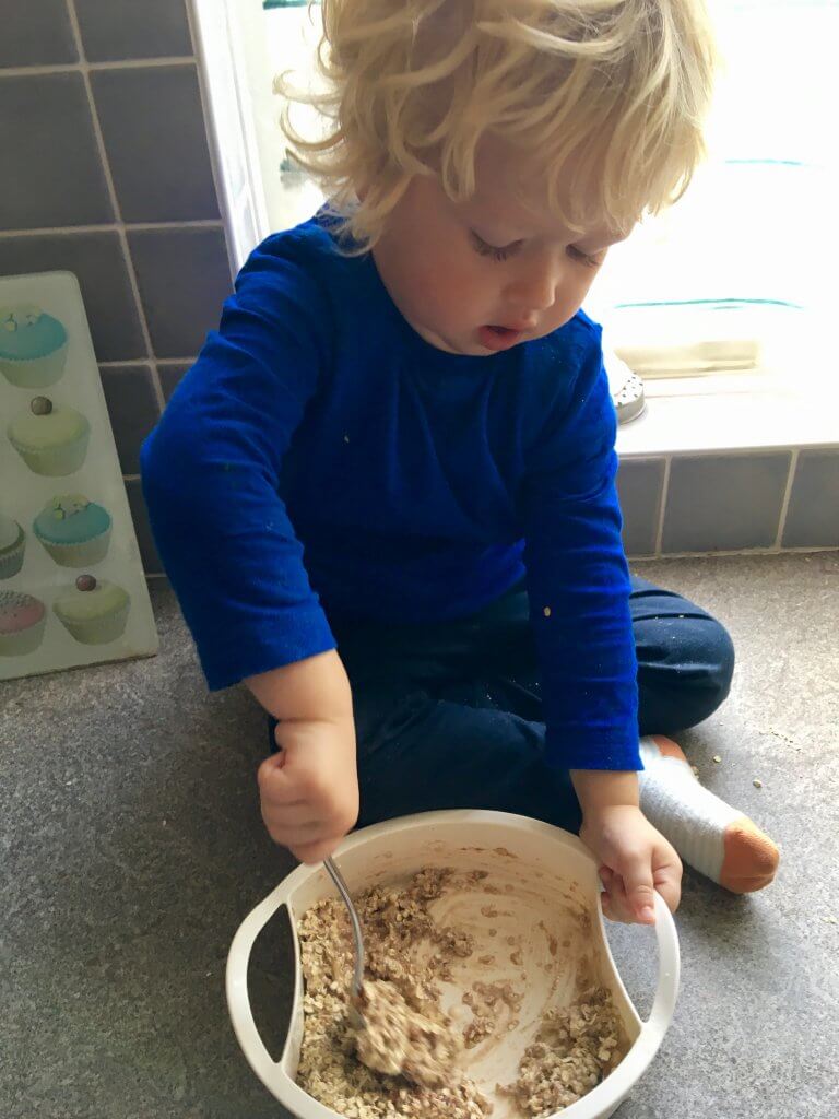 Savoury flapjack recipe Lucas is sat on a grey worktop stirring oats in a bowl