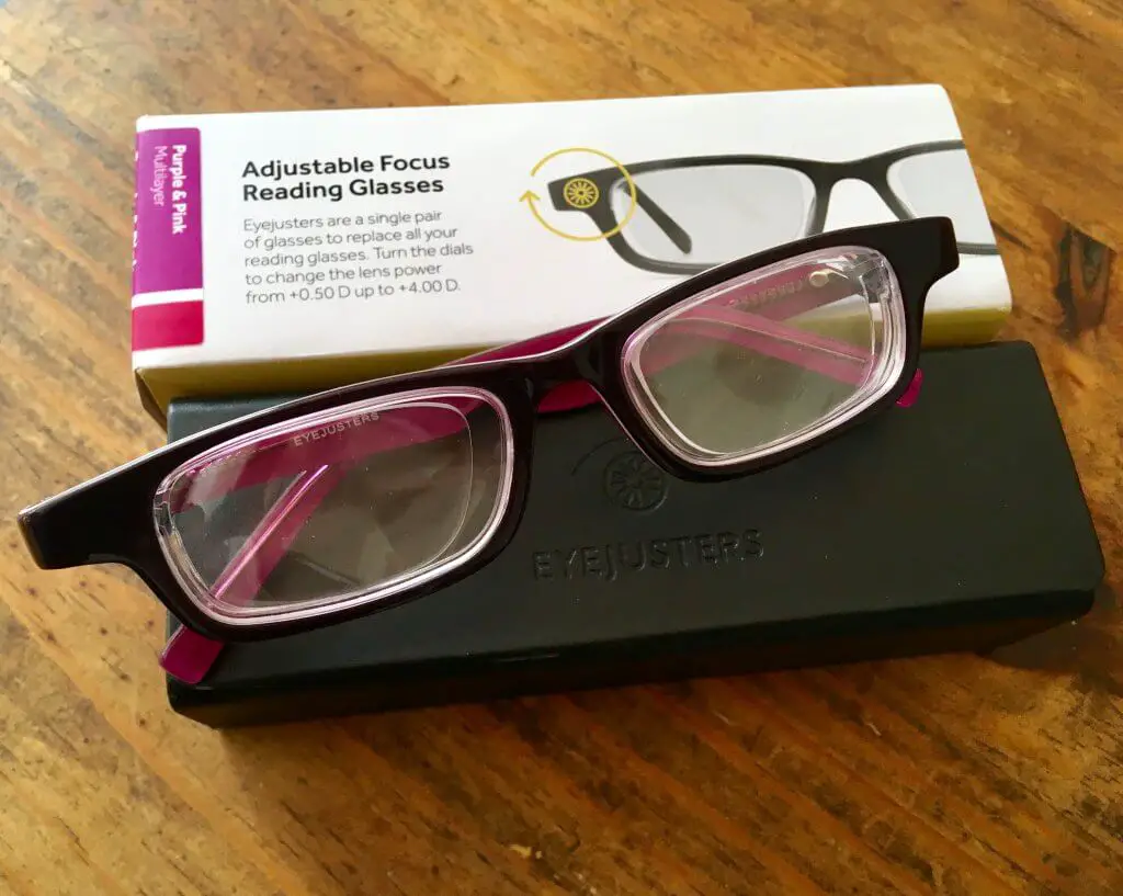 Eyejusters review purple glasses against a black case with white packaging on a wooden backfround