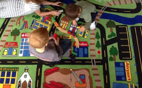 Choosing the perfect rug for your child’s playroom Two boys playing on a large rug that has the design of a road to play with cars on