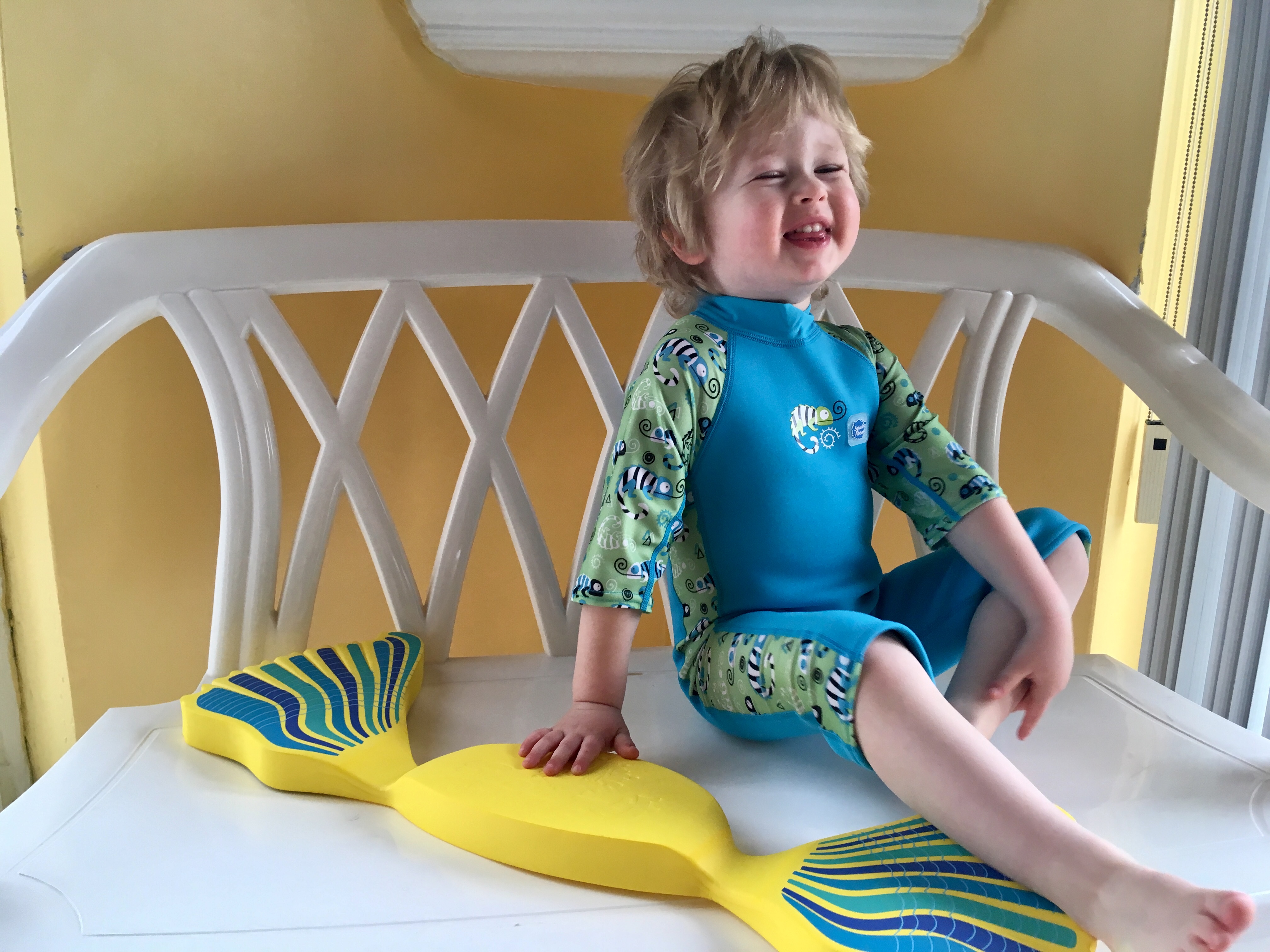 The benefits of learning to swim at a young age. Lucas sat in a bench laughing wearing a blue and green all in one sun suit
