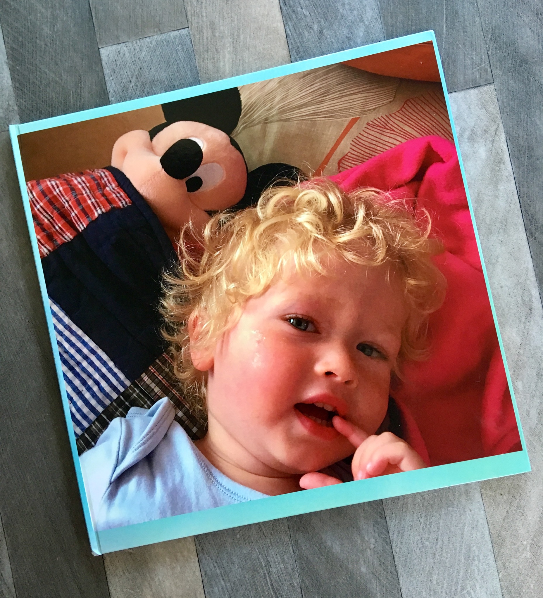 My-Picture.co.uk photo book. A photo of the front cover of the photo book showing Lucas looking up with blonde curly hair and a Mickey Mouse teddy next to him