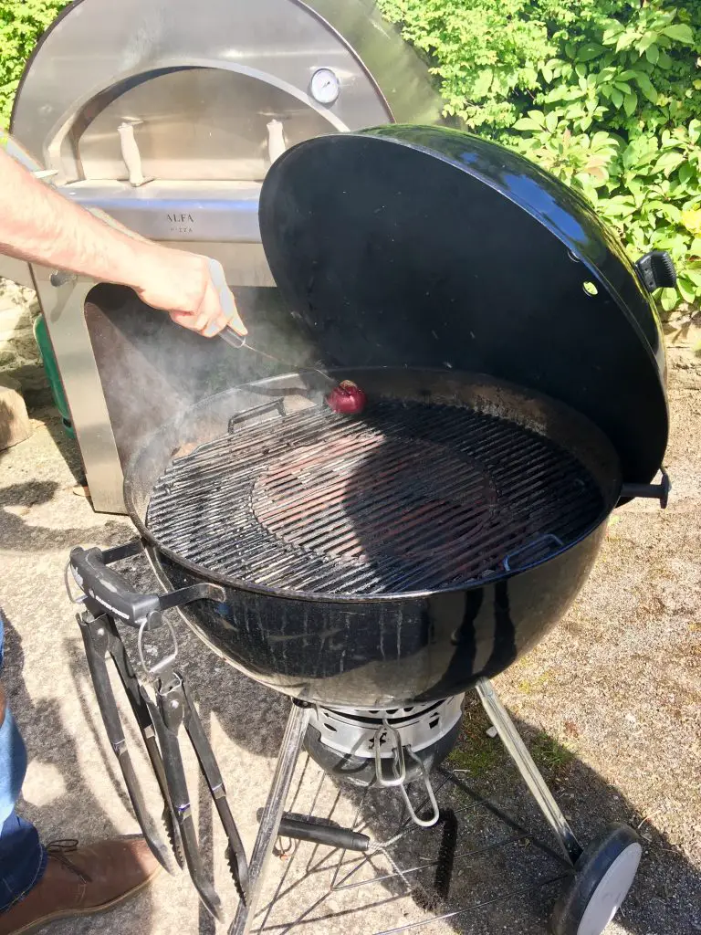 BBQ masterclass a kettle barbecue with someone greasing it with half a red onion held with a skewer