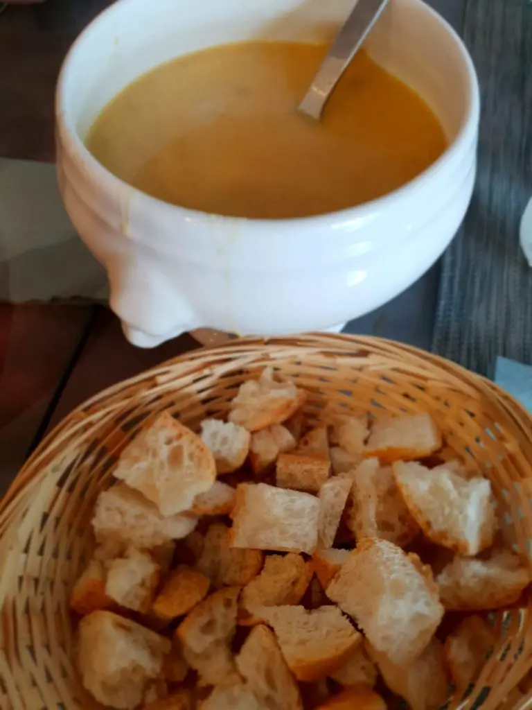 Ange and Lo Villamblard review vegetable soup in a serving bowl with a basket of fresh croutons 