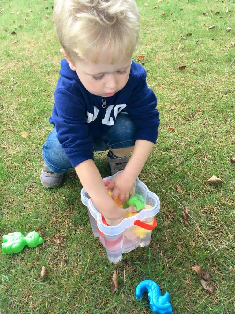 Celebrating outdoor play, every day Lucas is knelt down with his hands in a bucket of water playing with plastic toys 