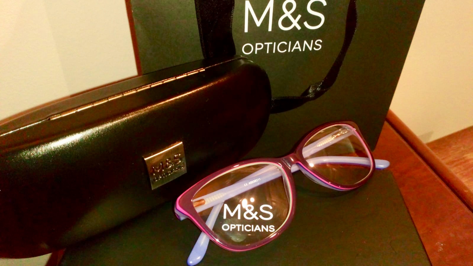 Marks and Spencer’s Opticians purple glasses next to a branded Marks and Spencer’s black glasses case and bag