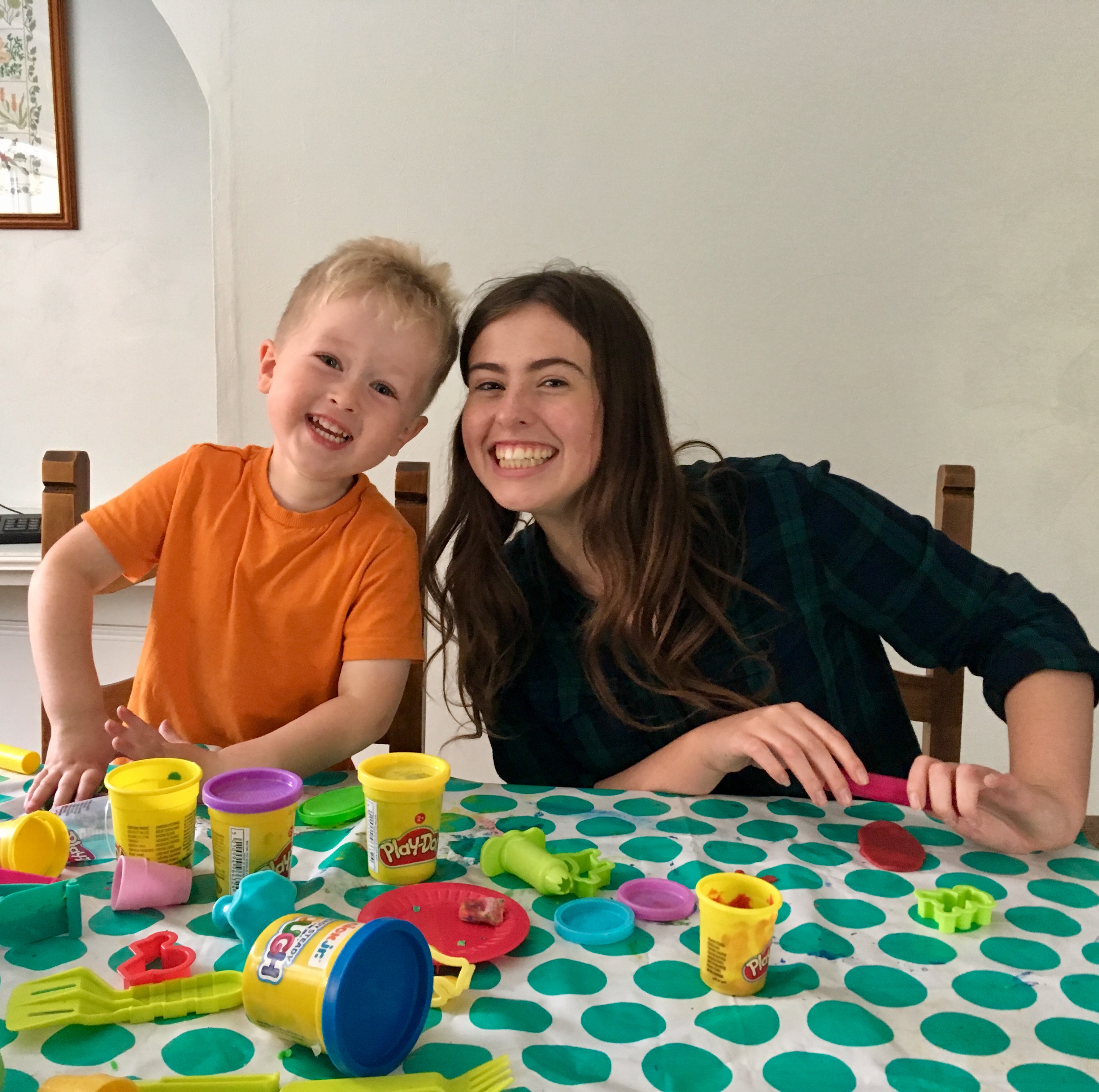 Lucas and his godmother sat at a table with play doh in front of them. They are both smiling at the camera