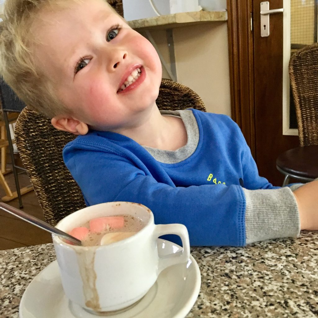Lucas sat in a cafe smiling at the camera with a hot chocolate in front of him