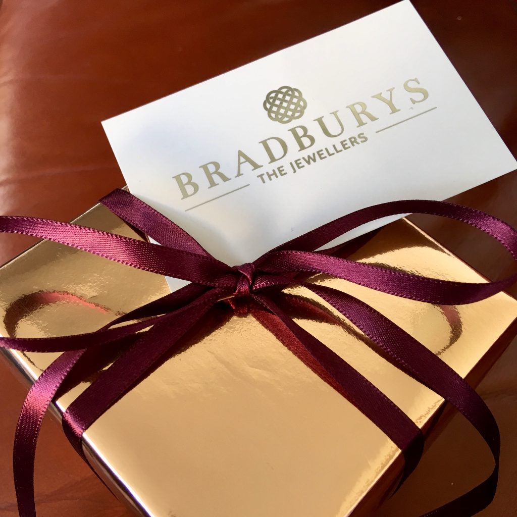 Bradbury's The Jewellers review. A gold gift wrapped box with burgundy ribbon tied round in bow with white and gold embossed business card