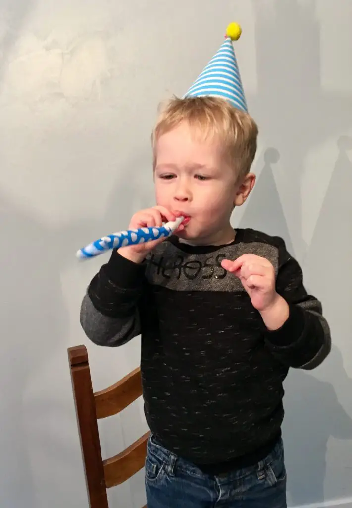Peppa Secret Surprise review Lucas with a blue and yellow party hat on, blowing a party blower and wearing a black jumper