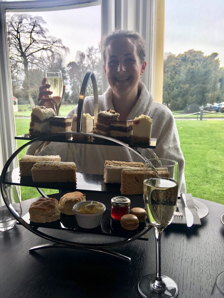 The Club and Spa Chester I am sat behind the afternoon tea stand smiling holding a glass of Prosecco 