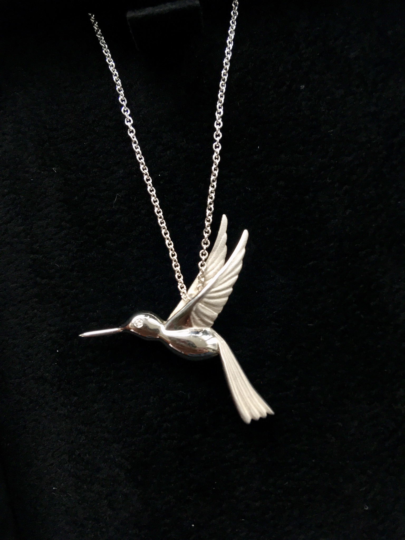 Ingle and Rhode review - the ethical jeweller. Close up of silver hummingbird necklace with diamond eye against a black felt background