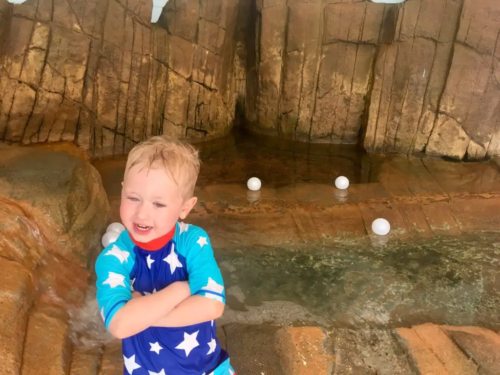 Lucas is stood smiling with his arms folded next to a rock pool