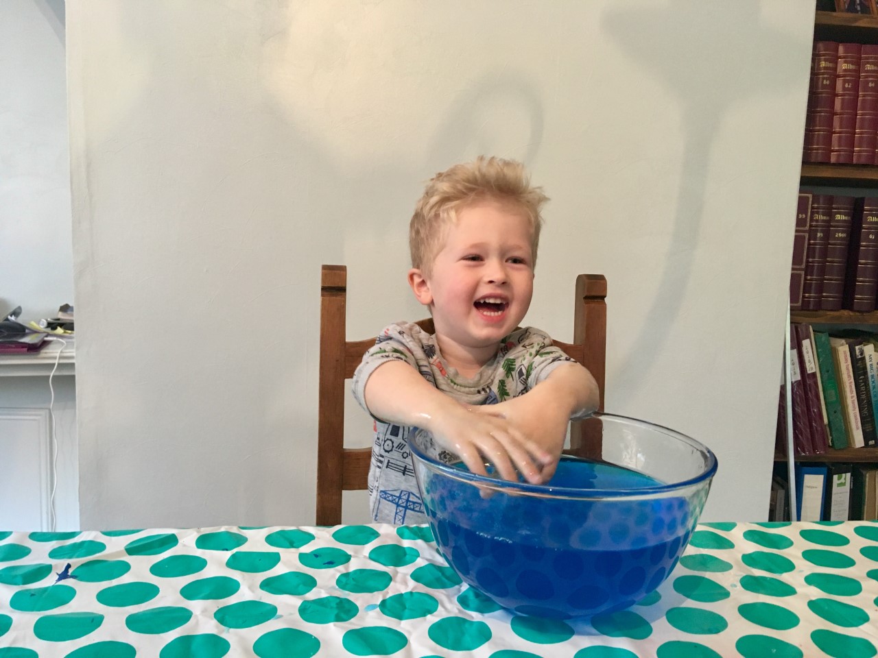 Lucas is sat at table with his hands in a big bowl of blue slime