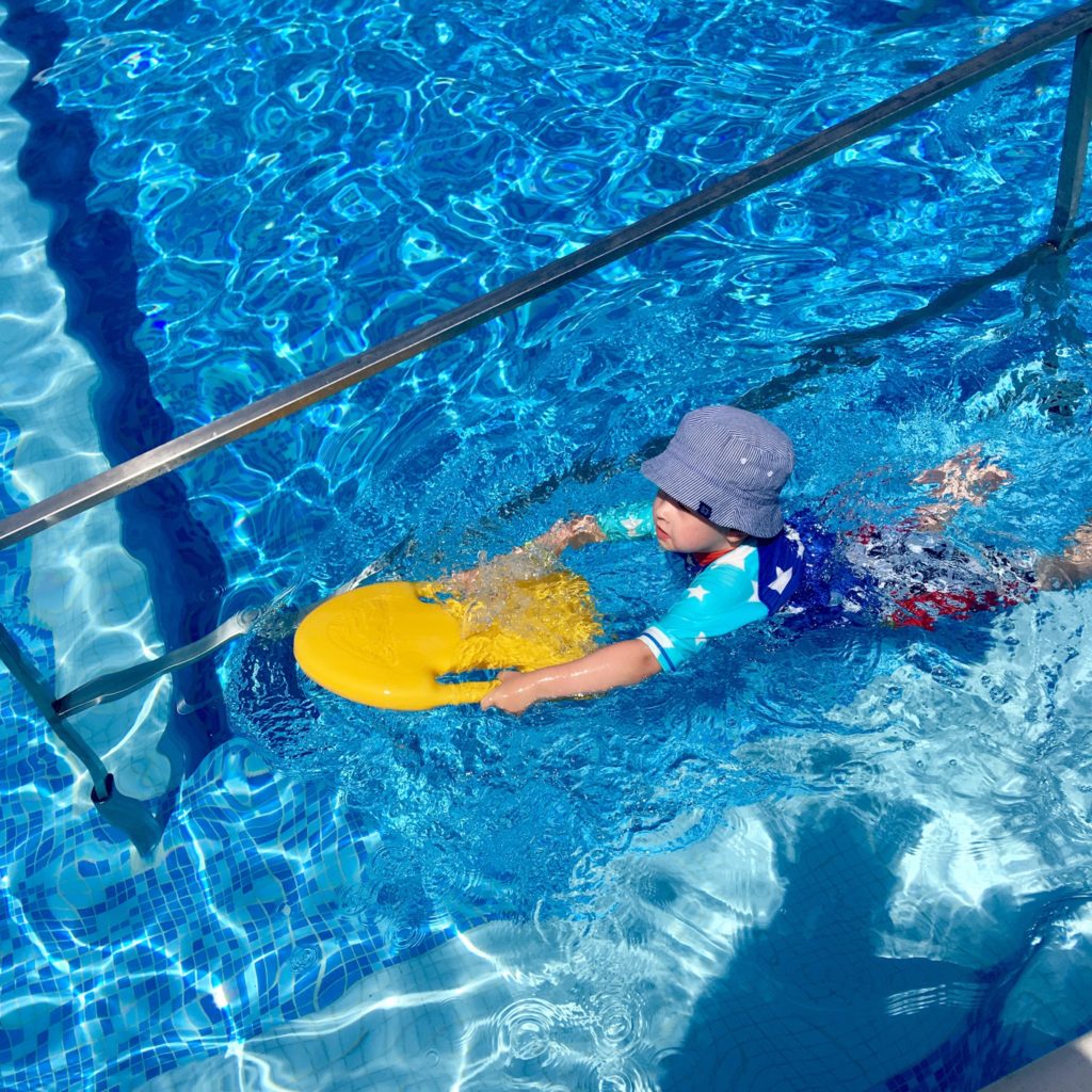 Lucas is swimming in the pool holding onto a yellow float