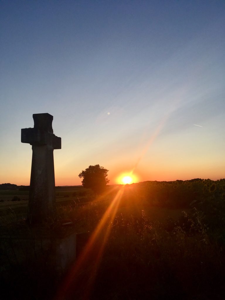 Sunset over a field, you can see a cross statue to the left of the photo 