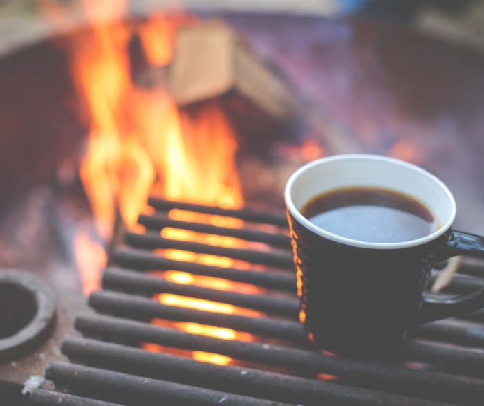 a cup of coffee and an outdoor fire in the background