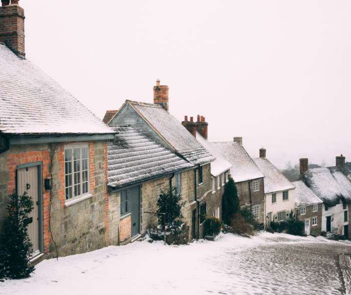 a cobbled street covered in snow with houses along the side
