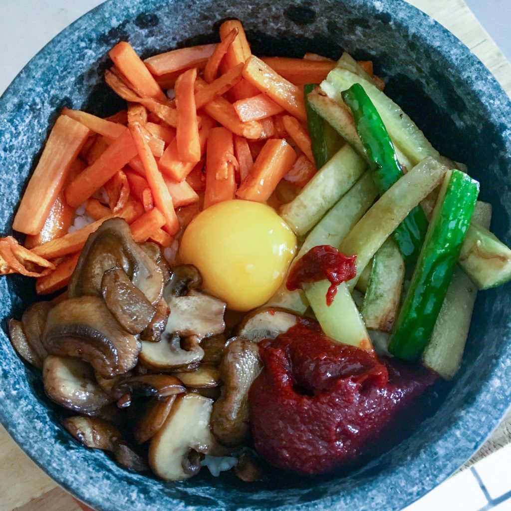 The Korean dolsot bibimbap cooked shown in the bowl with ingredients arranged in a circle and the egg in the middle 