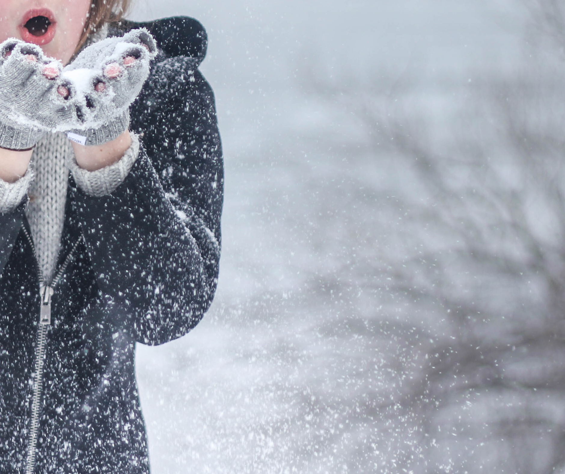 a lady in a black coat and gret fingerless gloves blowing snow from her hands