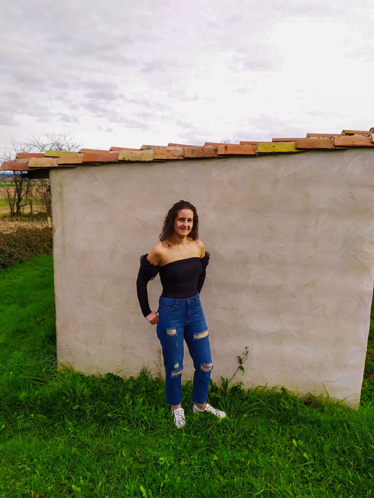 I stood outside next to a bricked building wearing ripped jeans and black mesh Bardot top from femme luxe