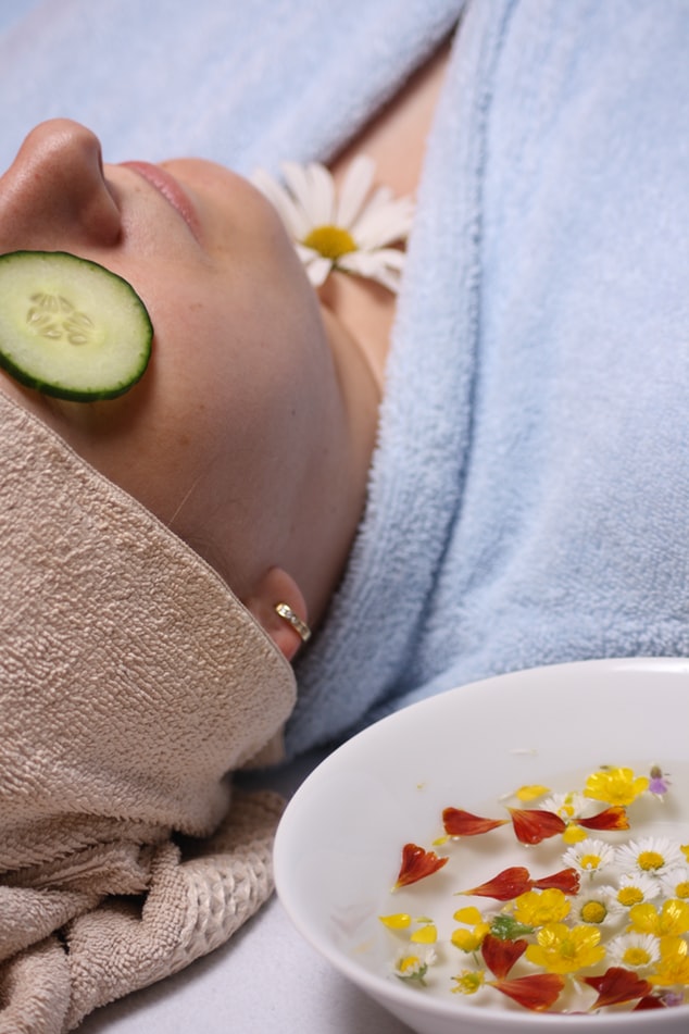 a lady led down with cucumbers on her eyes, a towelling robe around her and bowl of water next to her with flowers in it