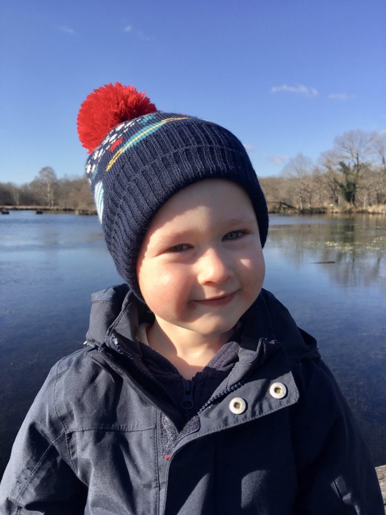 Lucas looking at the camera smiling wearing a navy and red bobble hat and navy coat