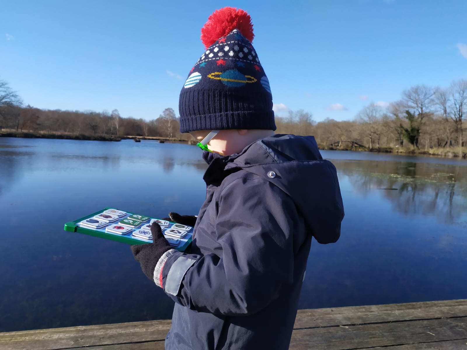 Lucas is side on to the camera. You can see a lake behind him. He is looking down at his magnet board