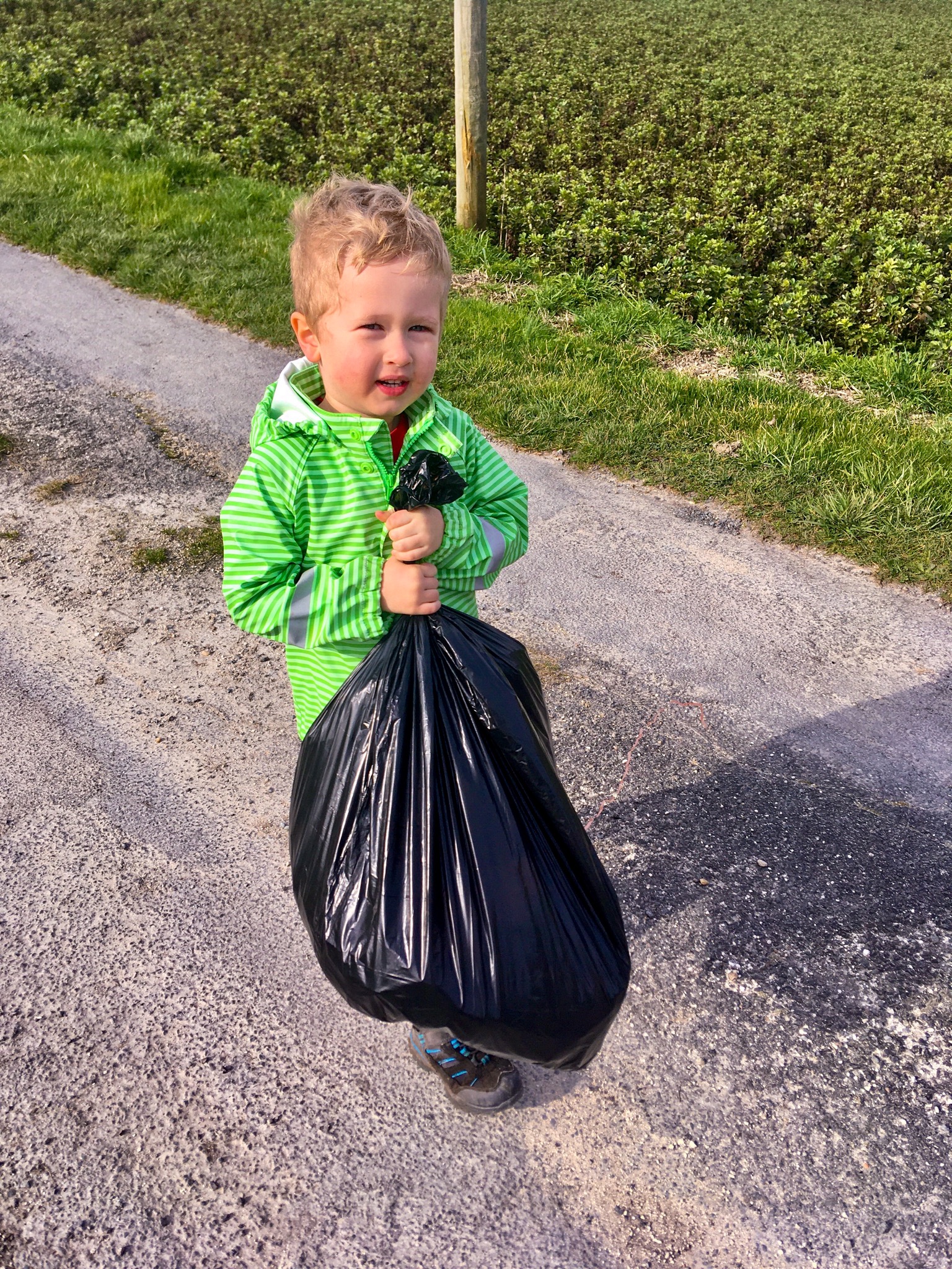 Lucas stood on a road holding the black bin bag wearing a green stripy coat
