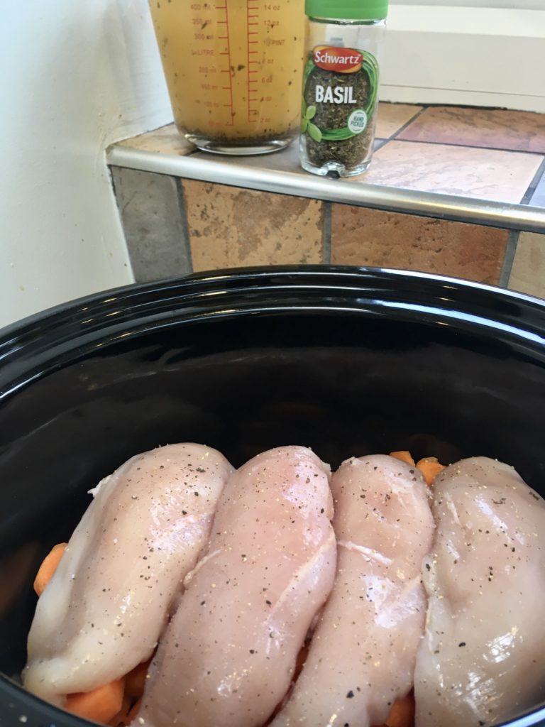 Four chicken breasts layered on top of carrots in the slow cooker 