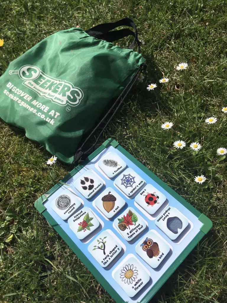 The seekers magnetic scavenger hunt board on grass near some daisies and the bag 