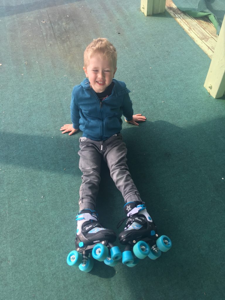 Lucas sat down smiling with his legs straight showing his turquoise and black roller skates 