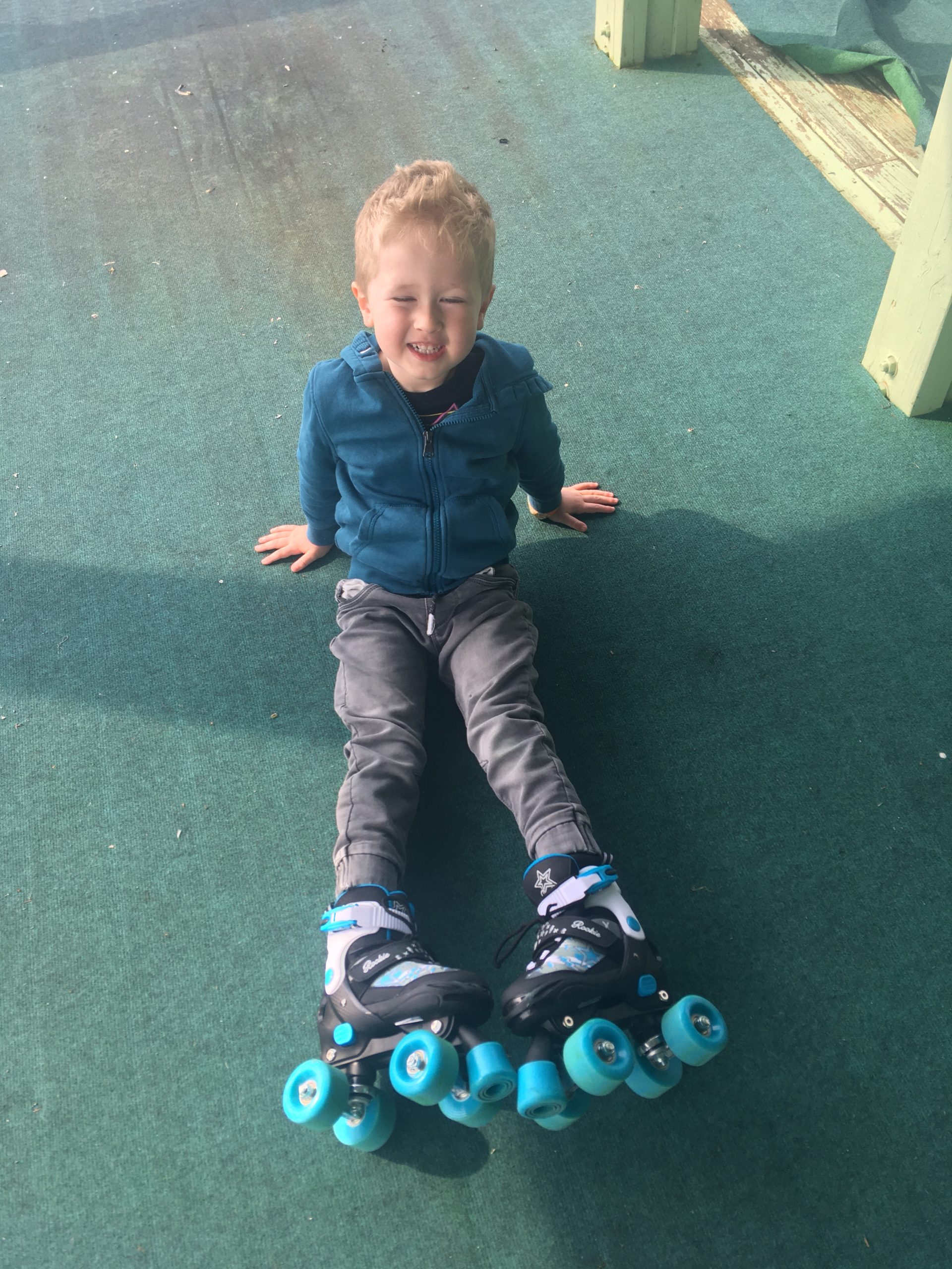 Lucas sat down smiling with his legs straight showing his turquoise and black roller skates