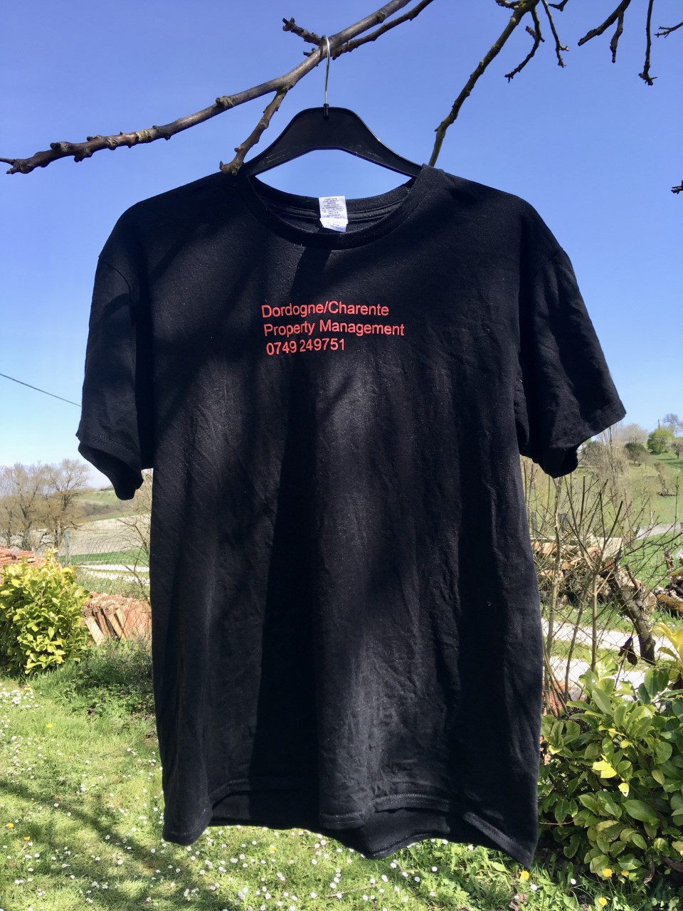 Getting the branding right with Printcious. The black tshirt with red writing. It is hung up on a branch of a tree overlooking countryside