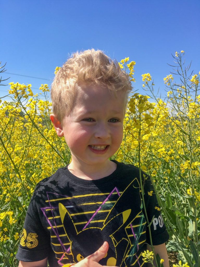 A close of of lucas smiling next to a yellow rapeseed field 