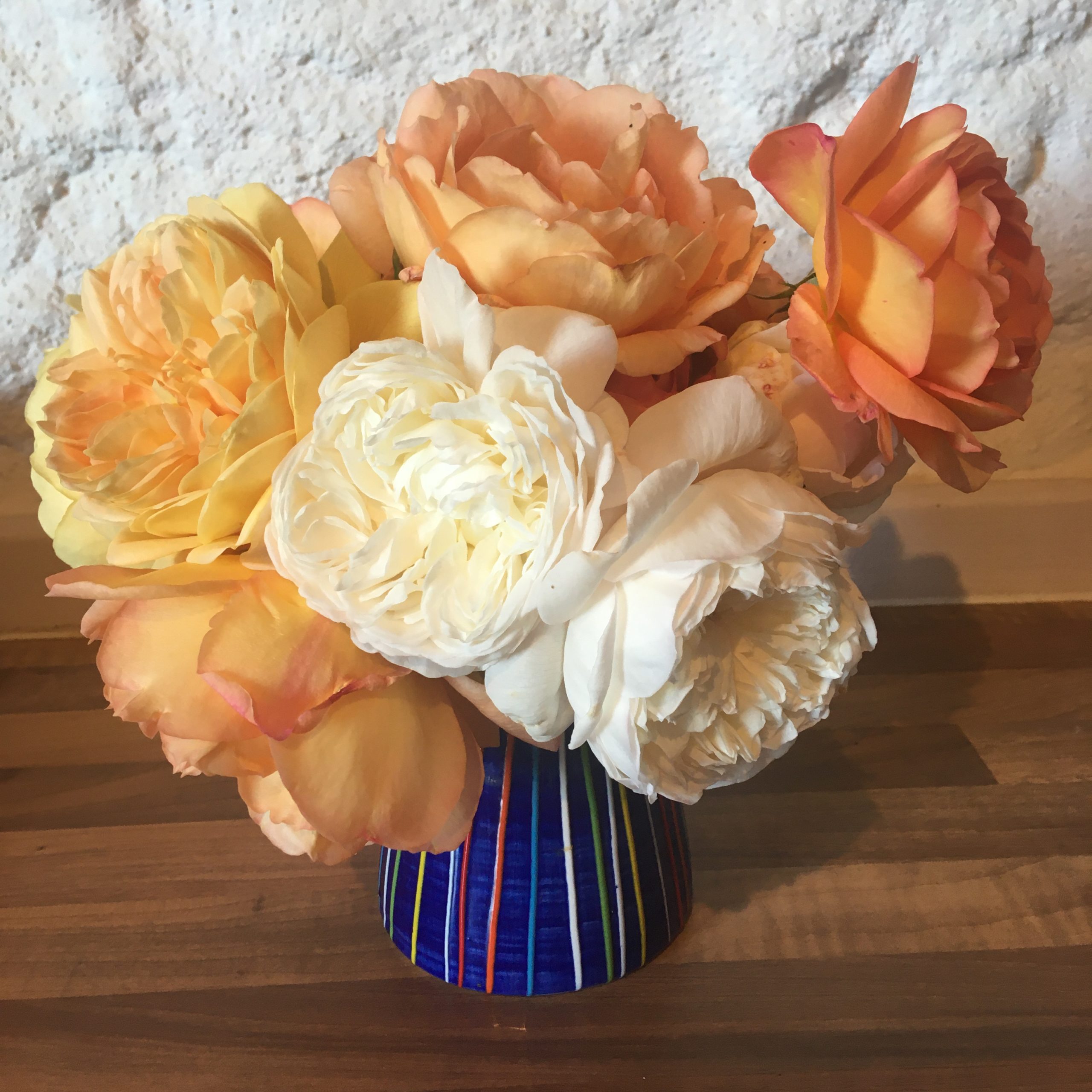 Peach yellow and cream flowers picked from the garden in a blue stripy vase