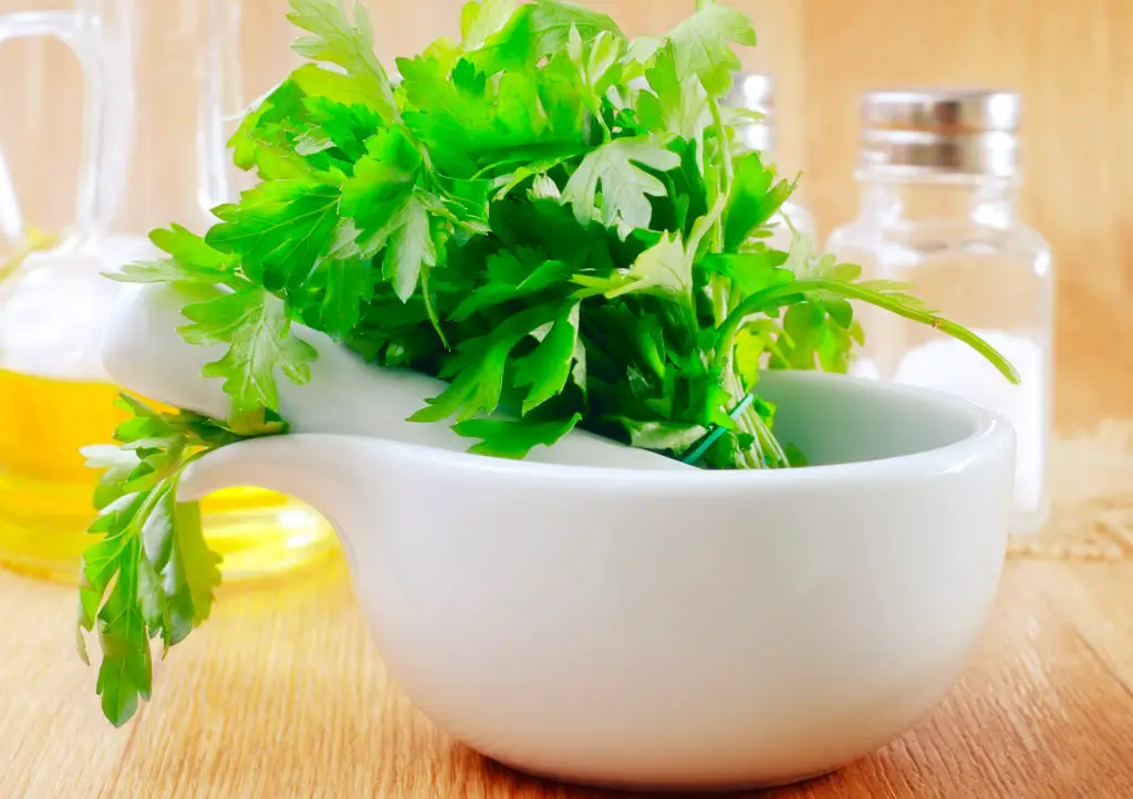 parsley leaves in a white bowl with bottles of oil behind