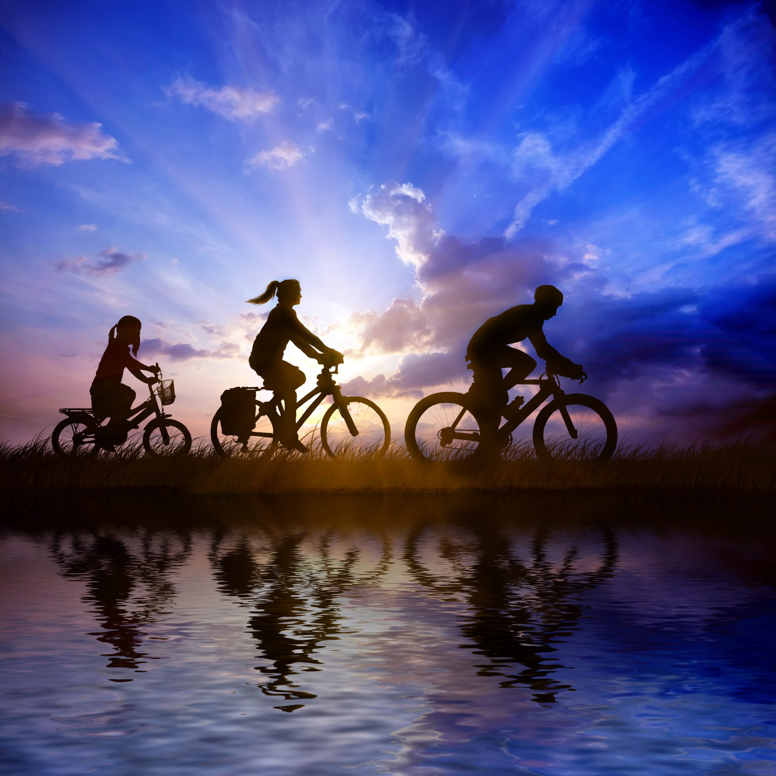 Going cycling with children. The photo shows two adults and a child cycling in the evening with a sunset behind
