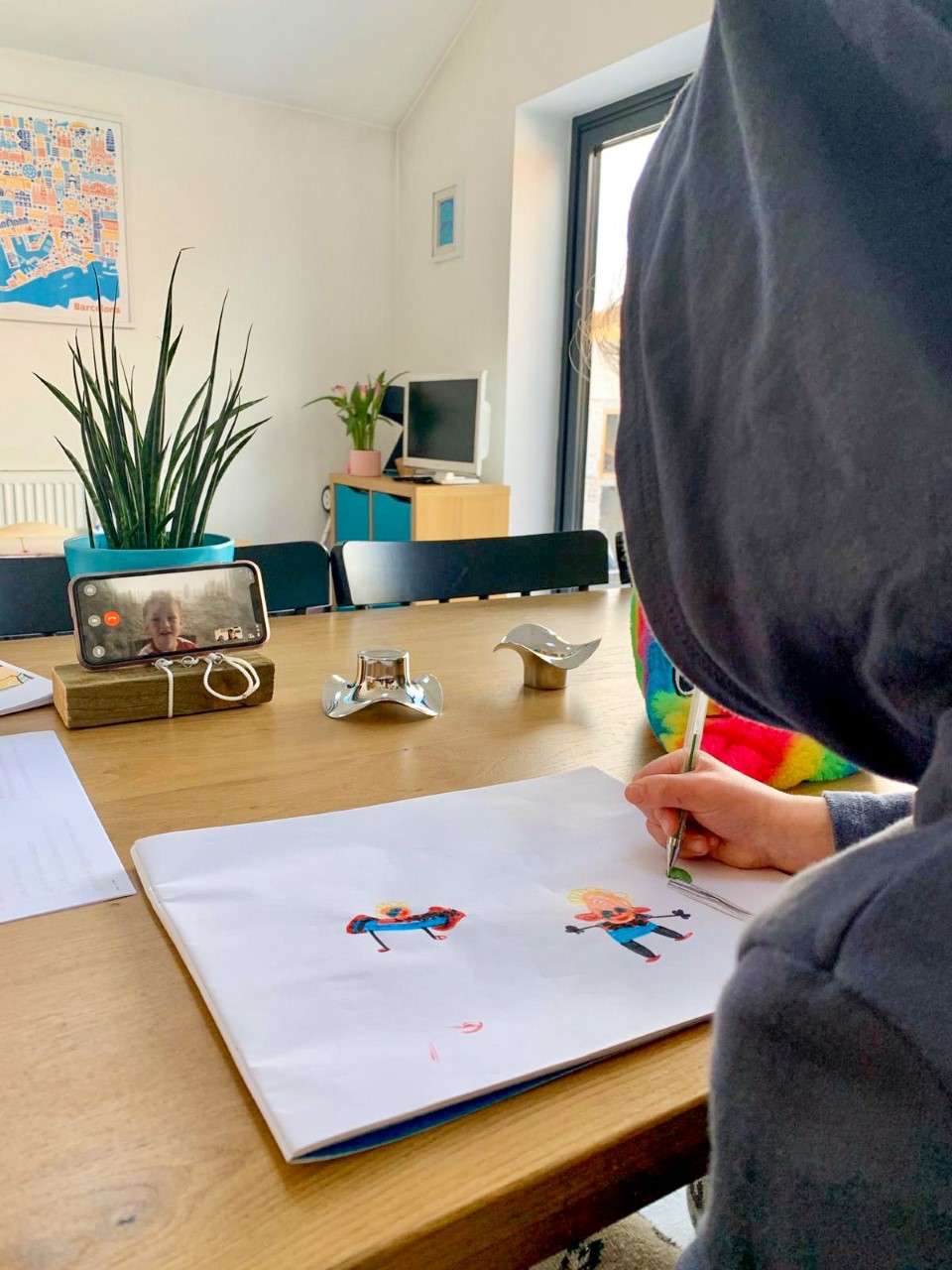 You can see the corner of Lucas' friend with her hood up. She is sat at a table drawing Lucas and Lucas is in the phone in front of her