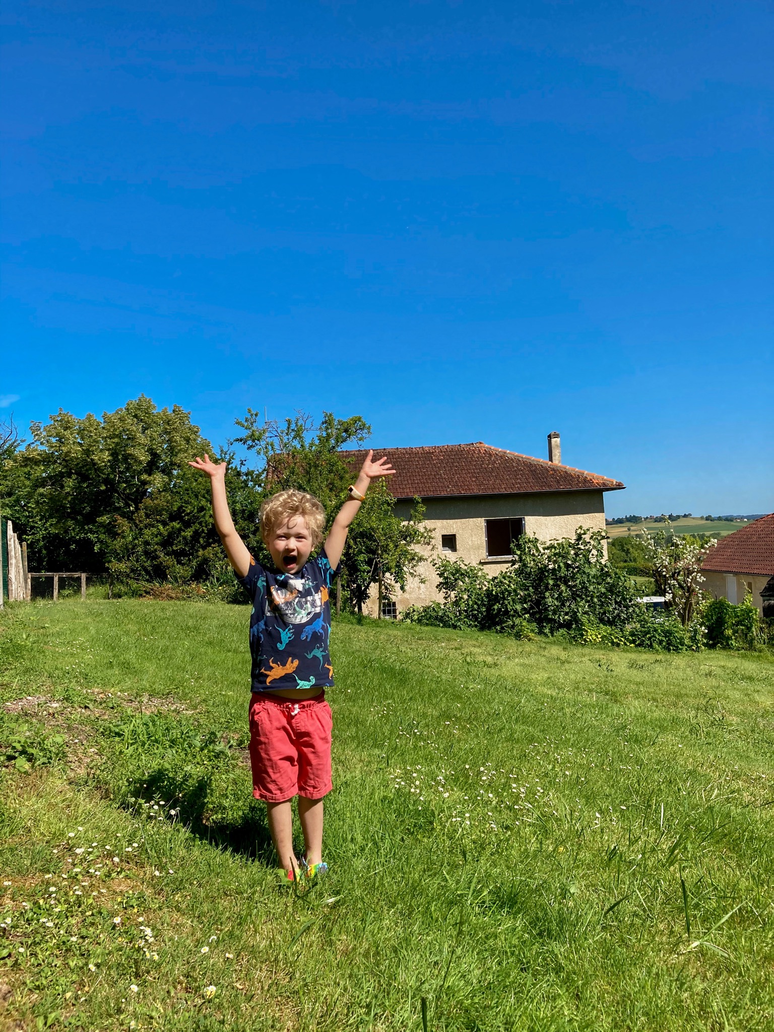 Lucas stood in the garden with his arms up and smiling. The house is in the background