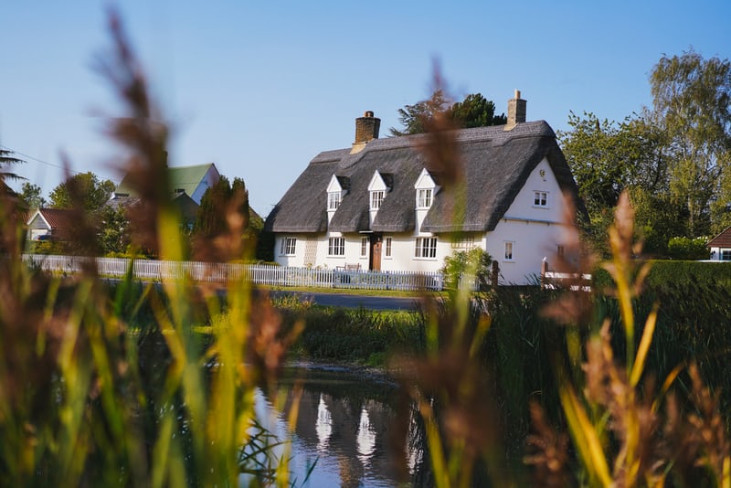 a white cottage with a thatched roof on the river side