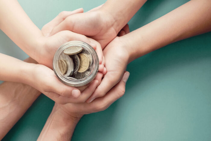 2 pairs of adult hands and a childs hands holding a jar of coins